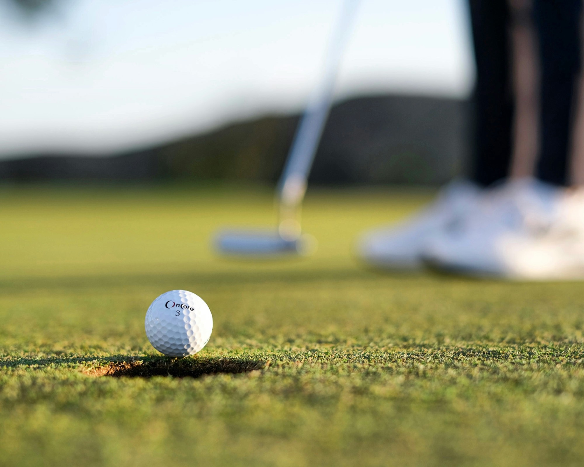 A golf ball rolling toward the cup on a practice green at golden hour